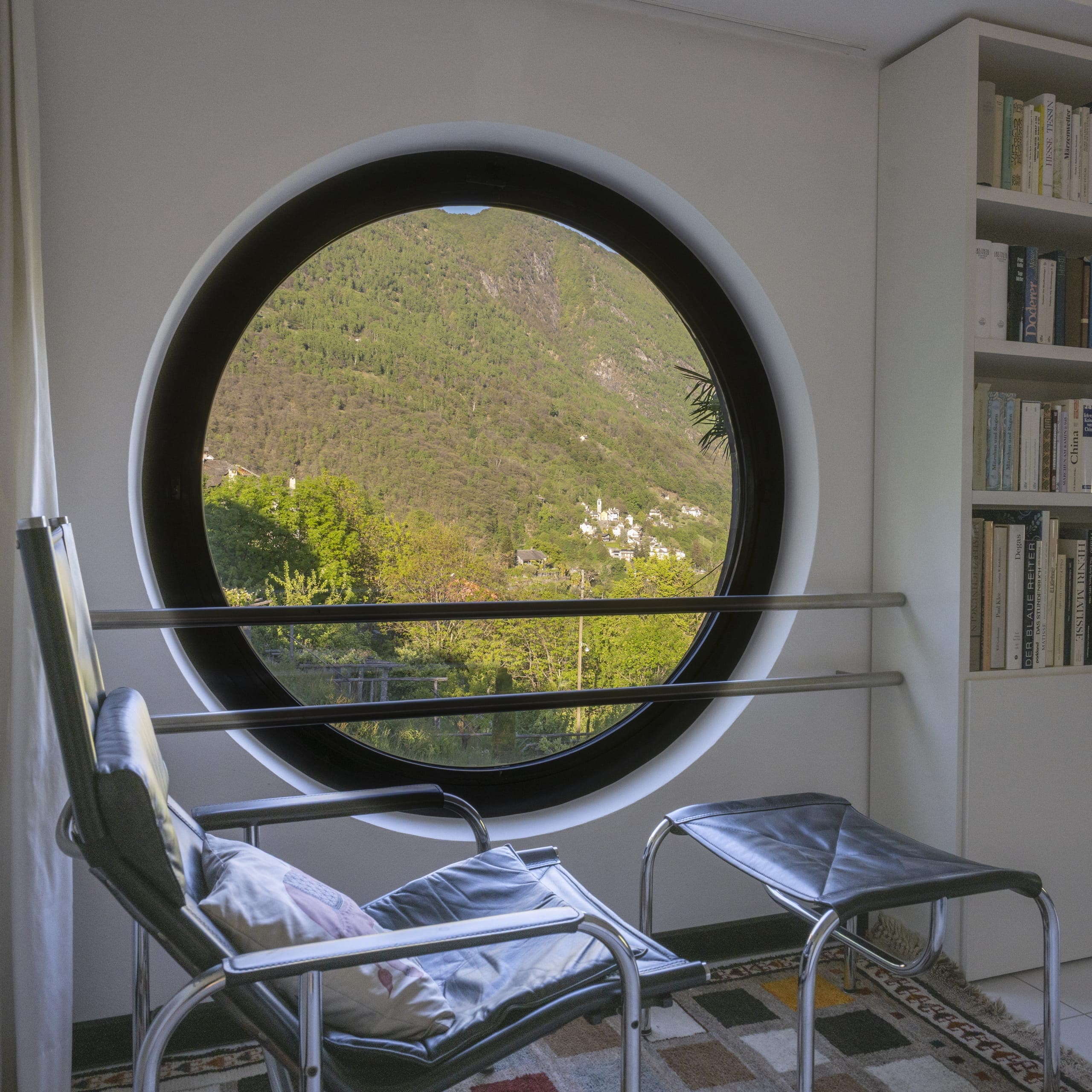 Rundes Fenster der Casa Walser mit Blick ins Grüne und reduziertem Sitzbereich